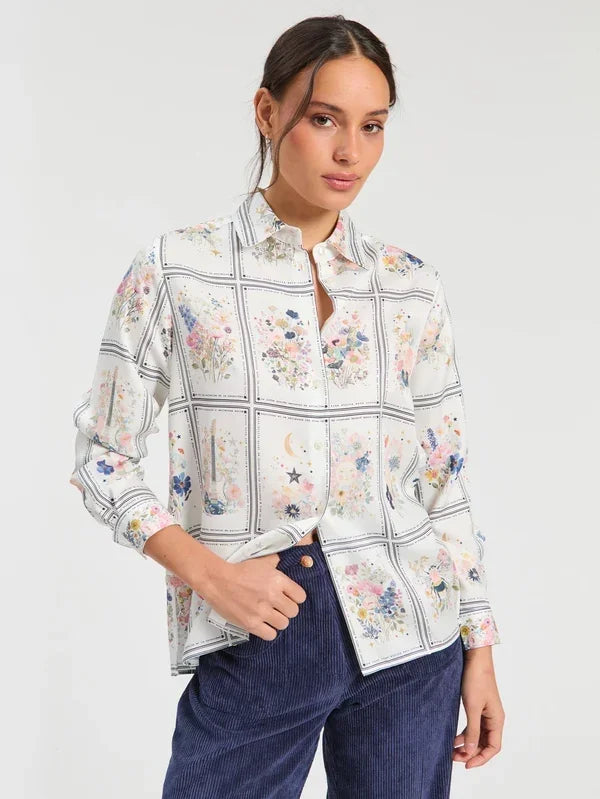Woman wearing a white long-sleeve floral print button-down shirt and navy corduroy trousers.