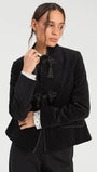 Woman wearing a luxury black velvet mandarin collar jacket with decorative tassel closures.