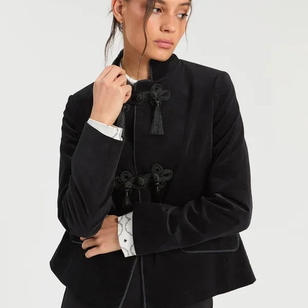 Woman wearing a luxury black velvet mandarin collar jacket with decorative tassel closures.