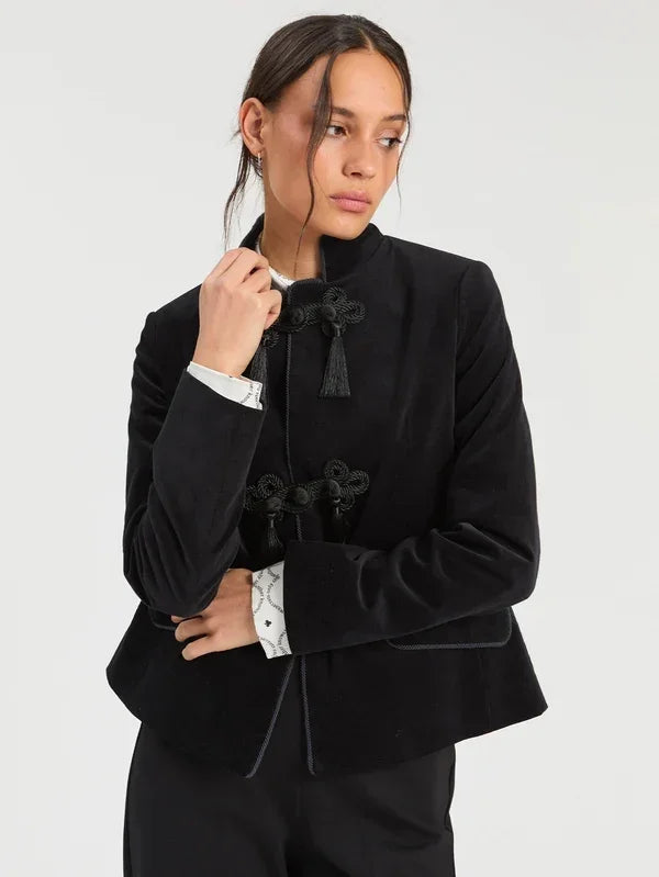 Woman wearing a luxury black velvet mandarin collar jacket with decorative tassel closures.