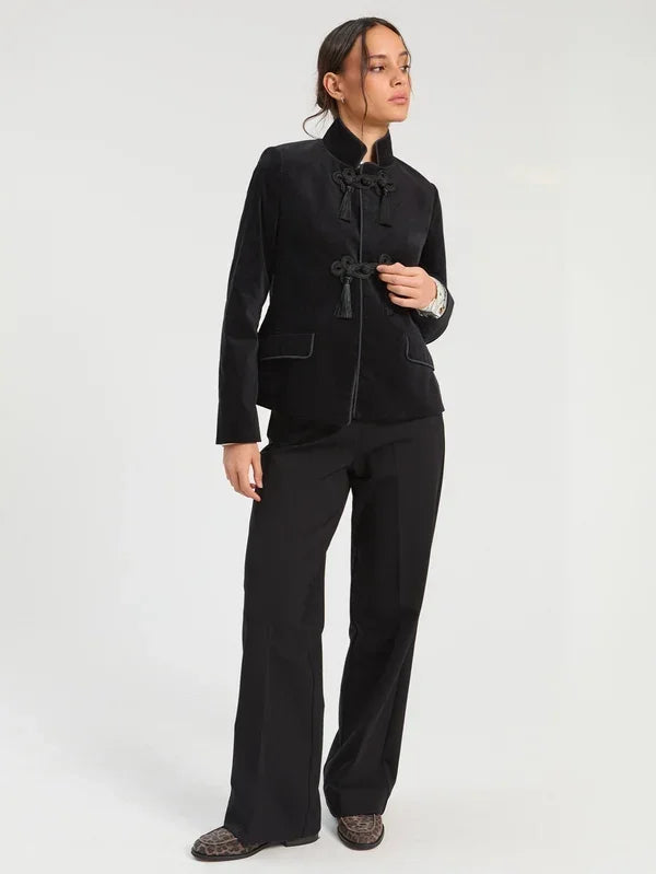 Woman wearing a black designer mandarin collar jacket with tassel closures and wide-leg trousers.
