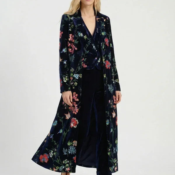 Woman wearing a luxury navy blue floral velvet long coat and matching wide-leg trousers.
