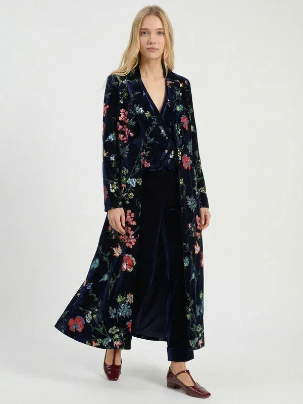 Woman wearing a luxury navy blue floral velvet long coat and matching wide-leg trousers.