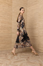 Woman in a black long-sleeve midi dress with gold and blue baroque pattern and gold heels.