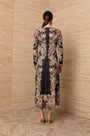 Back view of a woman wearing a long-sleeved black maxi dress with an ornate gold baroque print.