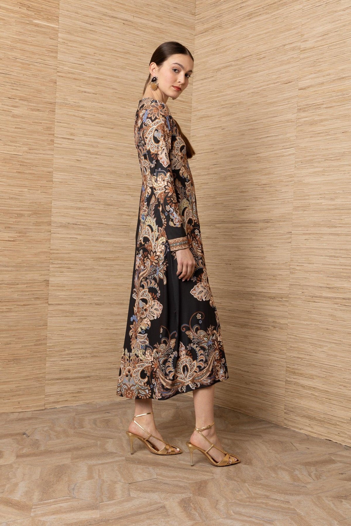 Woman wearing a long-sleeved black maxi dress with an intricate bohemian paisley print.