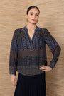 Woman wearing a patterned long-sleeve V-neck blouse and dark pleated skirt.