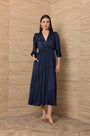 Woman wearing a navy blue satin midi dress with pleated skirt and gold heels.