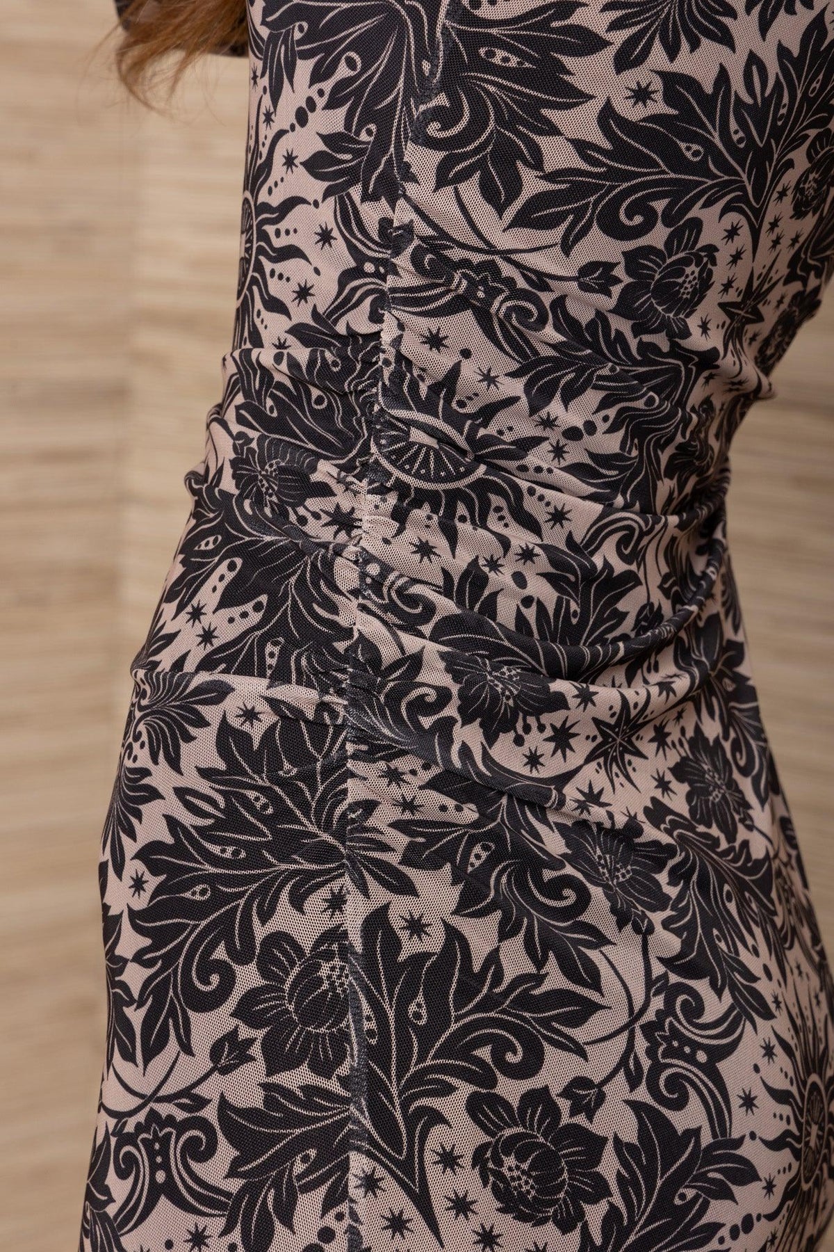 Woman wearing a luxury black and beige floral print ruched designer dress.