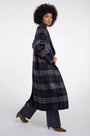 Woman wearing a long navy and brown plaid wool coat with wide-leg trousers.