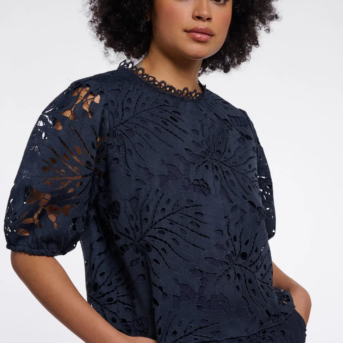 Woman wearing a navy blue laser-cut floral pattern blouse and matching trousers.