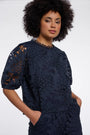 Woman wearing a navy blue laser-cut floral pattern blouse and matching trousers.