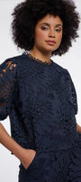 Woman wearing a navy blue laser-cut floral pattern blouse and matching trousers.