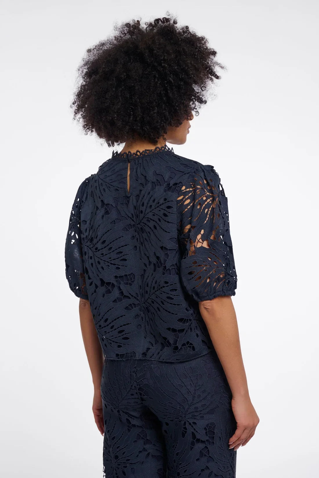 Back view of a woman wearing a navy blue laser-cut floral lace blouse and matching trousers.