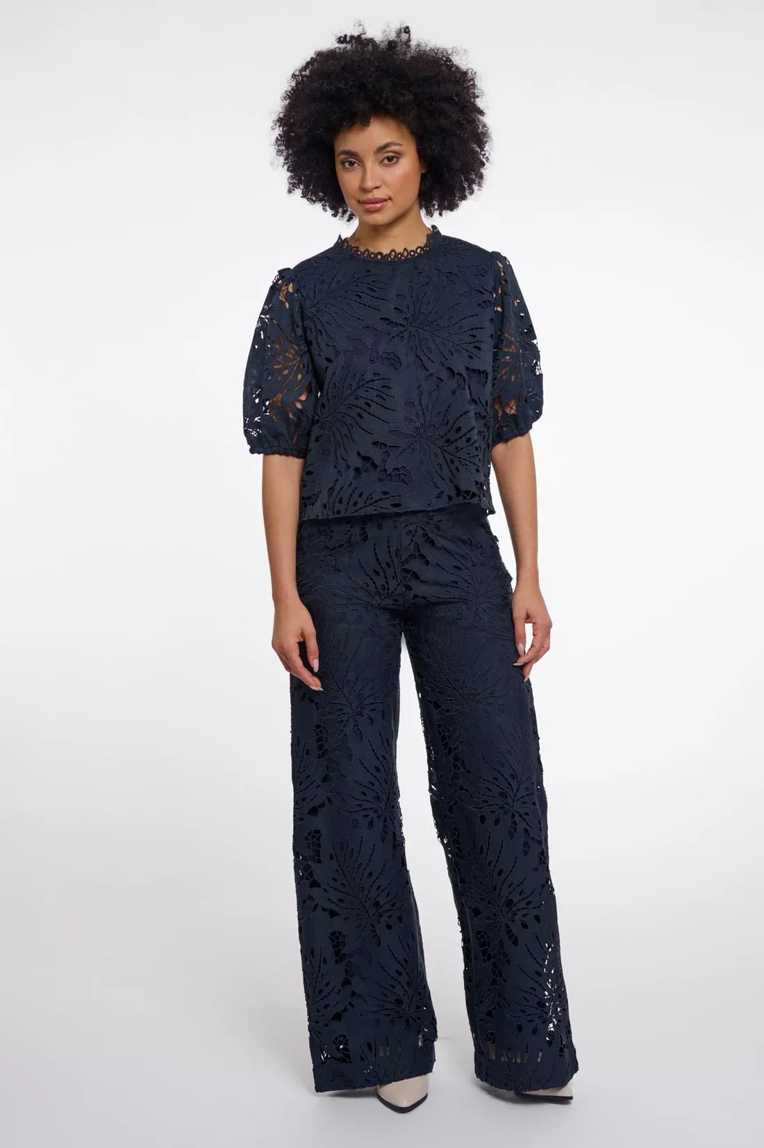 Woman wearing a navy blue lace two-piece set with a short-sleeve top and wide-leg trousers.