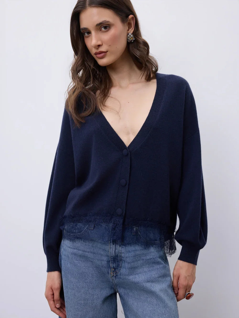 Woman wearing a navy blue v-neck knit cardigan with lace trim and blue denim jeans.