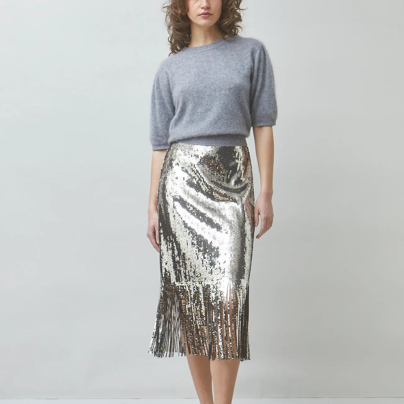 Woman wearing a grey knit sweater and a silver sequined midi skirt with fringe hem.