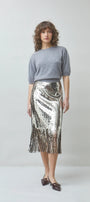 Woman wearing a grey knit sweater and a silver sequined midi skirt with fringe hem.