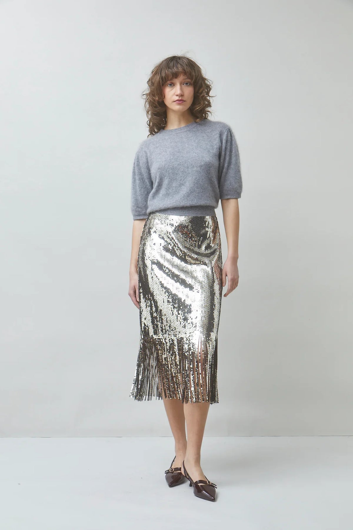 Woman wearing a grey knit sweater and a silver sequined midi skirt with fringe hem.