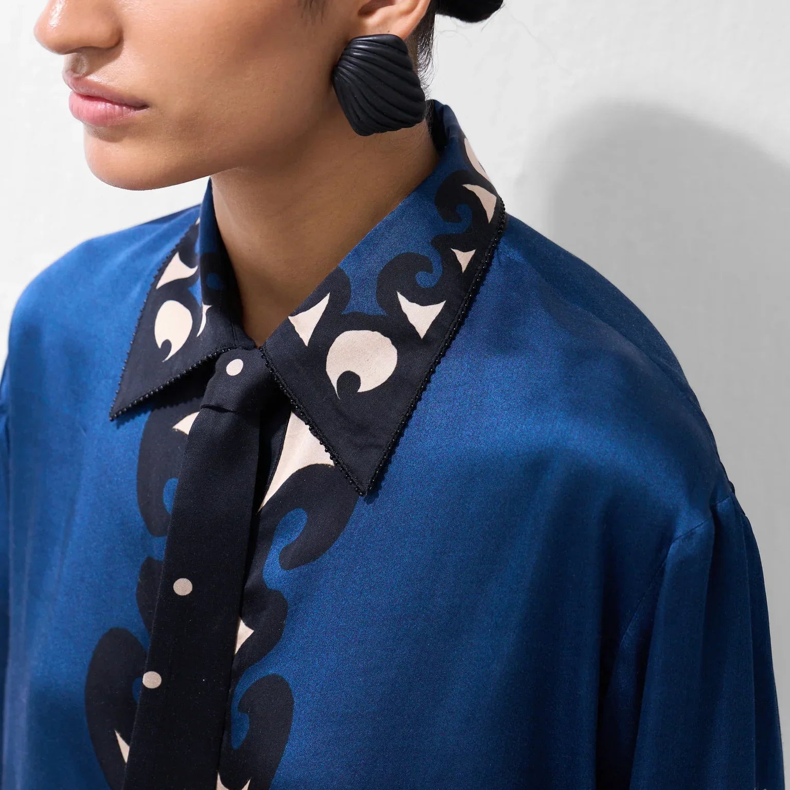 Woman wearing a blue silk patterned blouse and large black statement earrings.