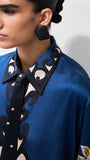 Woman wearing a blue silk patterned blouse and large black statement earrings.