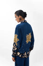 Woman in navy blue silk blouse with large gold floral patterns and decorative sleeve cuffs.
