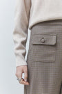 Woman wearing a cream knit sweater and brown houndstooth patterned skirt with pocket detail.