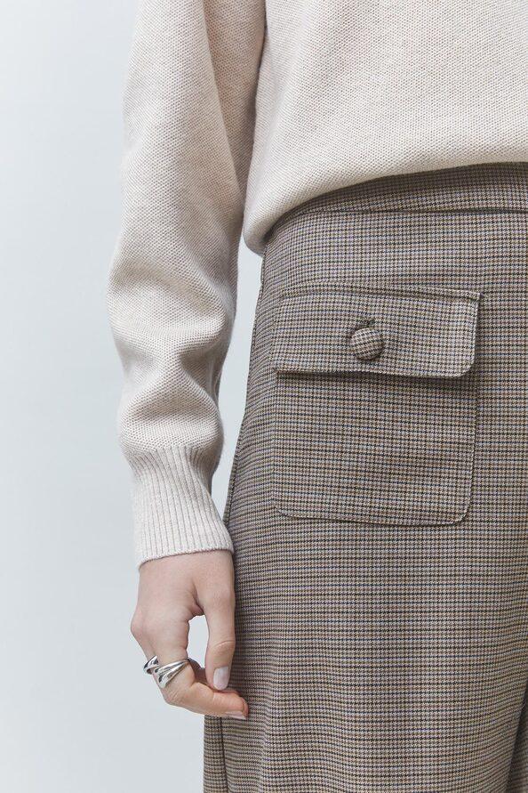 Woman wearing a cream knit sweater and brown houndstooth patterned skirt with pocket detail.