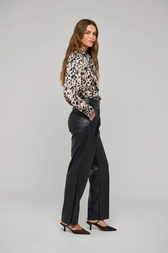 Woman wearing a leopard print blouse and black leather wide-leg trousers.