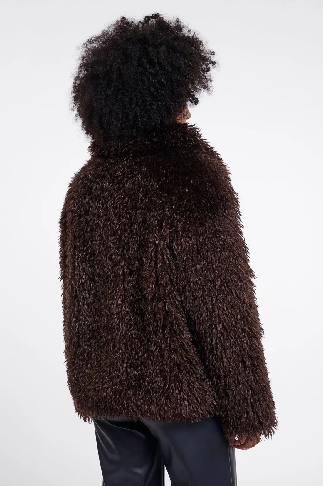 Back view of a woman wearing a brown faux fur jacket and black leather trousers