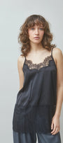 Woman wearing a black satin camisole with lace trim and matching trousers.