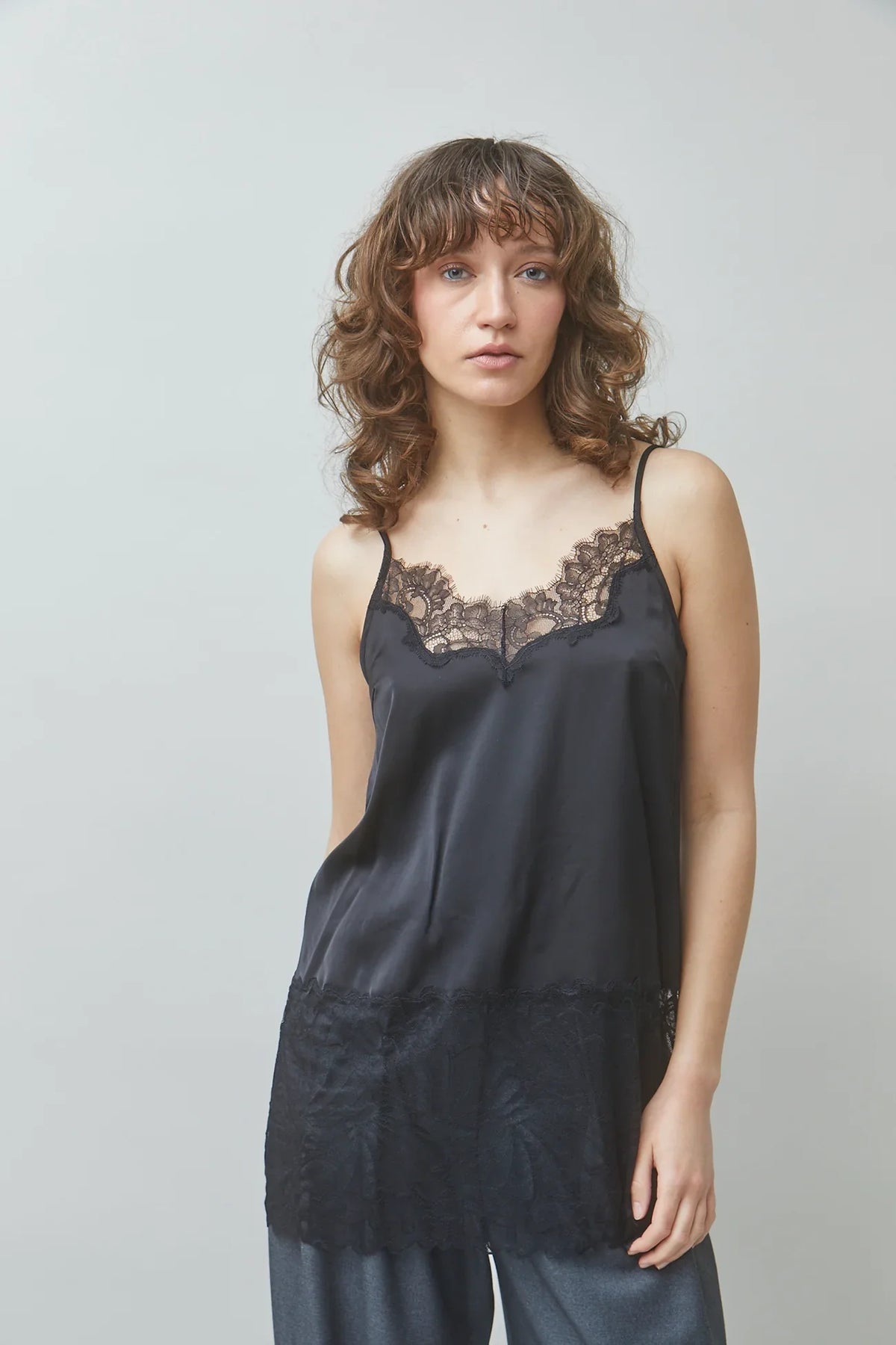 Woman wearing a black satin camisole with lace trim and matching trousers.