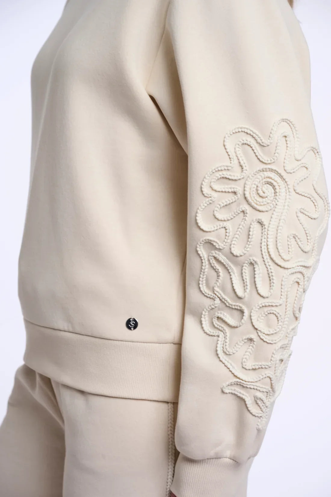 Cream designer sweatshirt with textured floral cord embellishment on the sleeve.