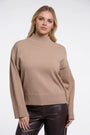 Woman wearing a luxury beige mock neck cashmere sweater and dark brown leather trousers.