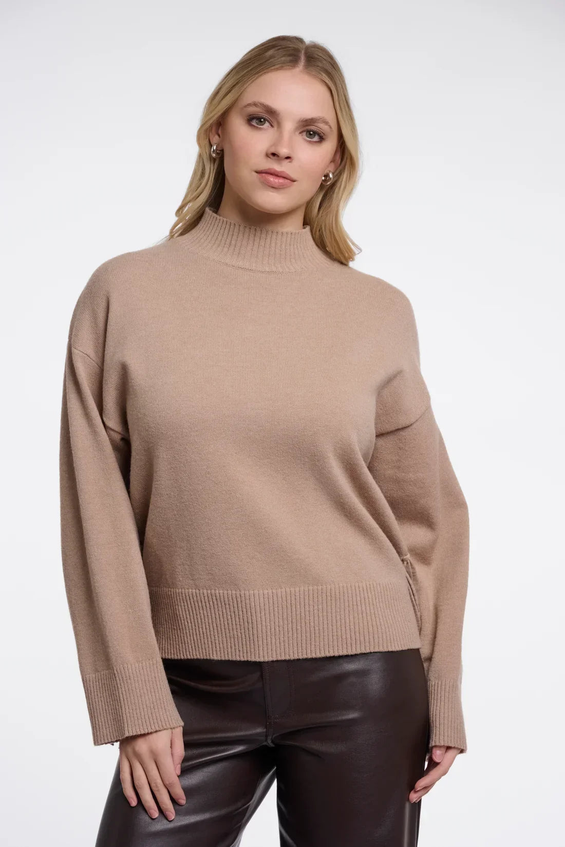Woman wearing a luxury beige mock neck cashmere sweater and dark brown leather trousers.