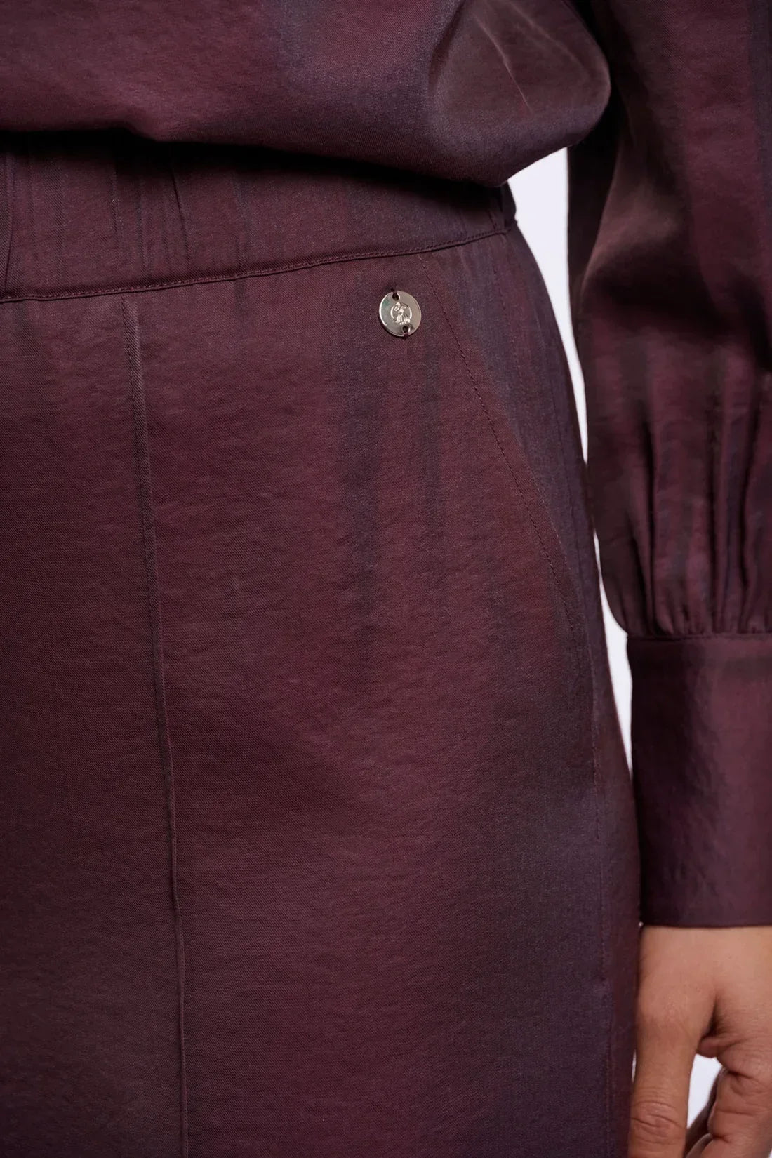 Close-up of luxury burgundy silk trousers with a silver button detail.