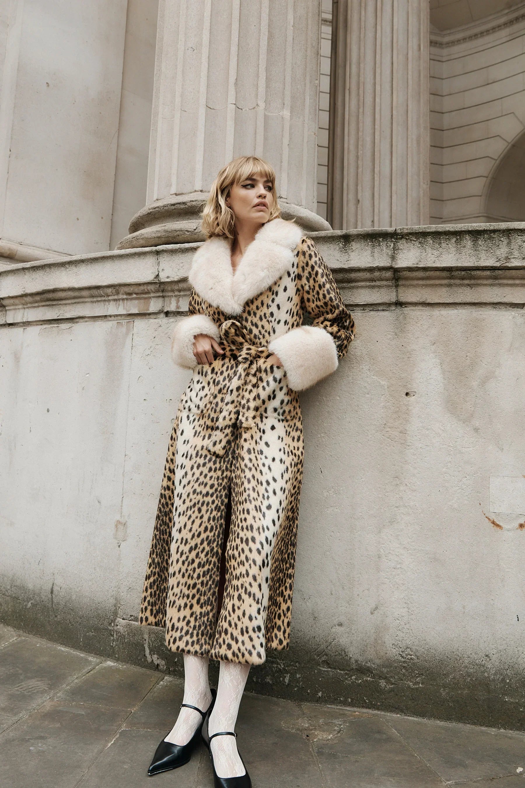 Woman wearing a luxury leopard print faux fur coat with cream trim and black heels.