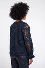 Back view of a woman wearing a navy blue floral eyelet lace blouse and dark leather pants.