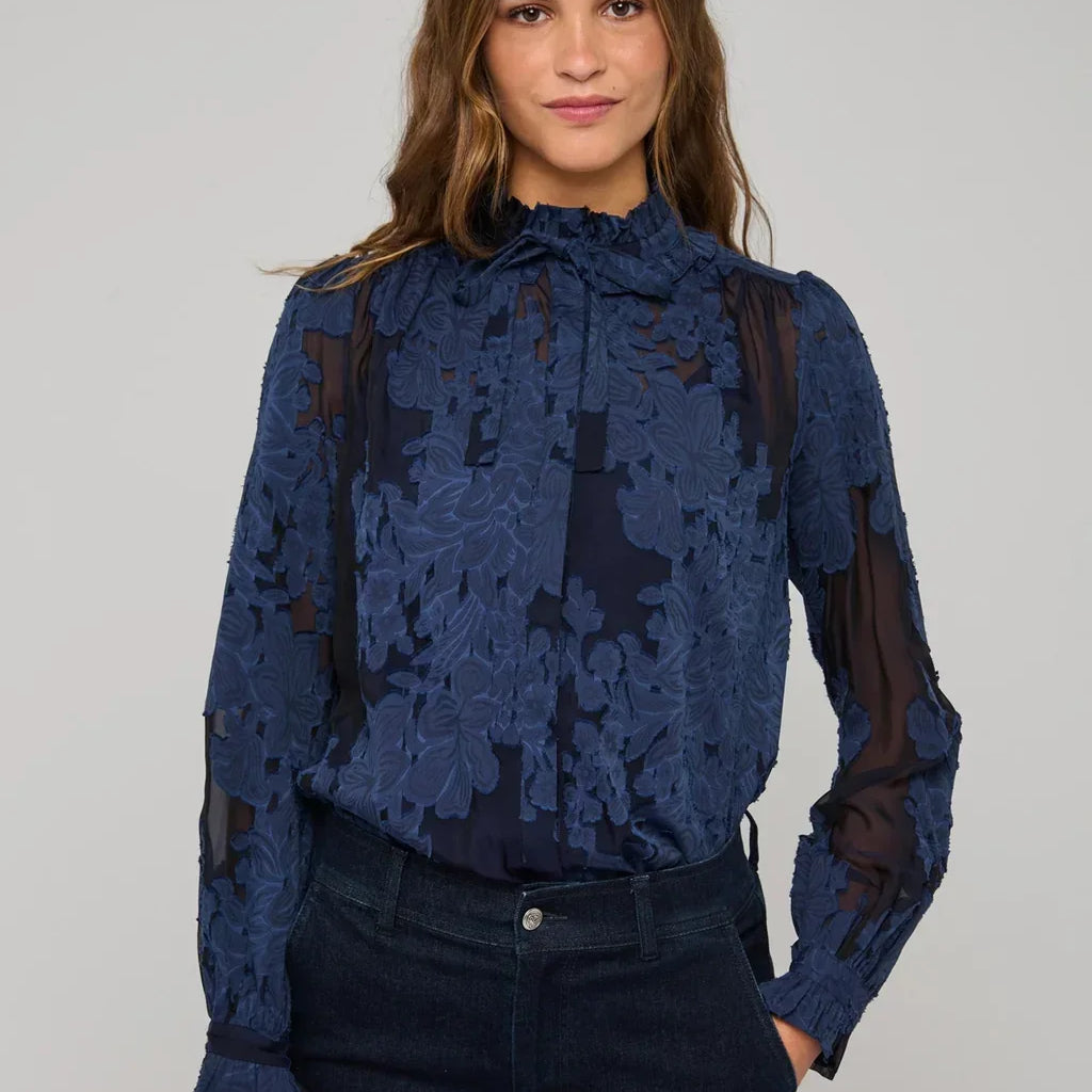 Woman wearing a navy blue floral lace long-sleeved blouse and dark denim jeans.