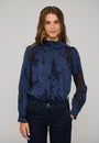 Woman wearing a navy blue floral lace long-sleeved blouse and dark denim jeans.