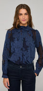 Woman wearing a navy blue floral lace long-sleeved blouse and dark denim jeans.