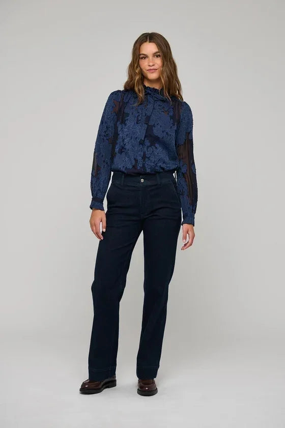 Woman wearing a blue floral textured blouse and navy blue trousers.