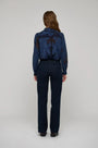 Back view of a woman wearing a blue floral lace blouse and dark navy wide-leg trousers.