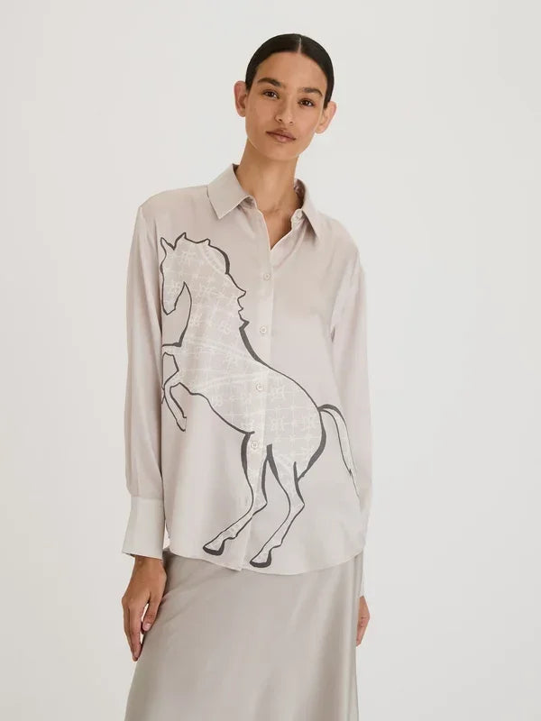 Woman wearing a beige long-sleeve silk shirt with a large black horse graphic print.