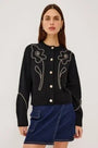 Woman wearing a black button-up cardigan with white floral embroidery and a blue denim skirt
