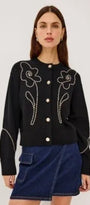 Woman wearing a black button-up cardigan with white floral embroidery and a blue denim skirt