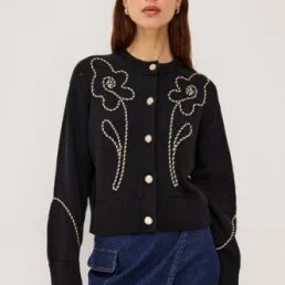 Woman wearing a black button-up cardigan with white floral embroidery and a blue denim skirt