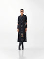 Woman wearing a long black designer coat with celestial and floral embroidery.