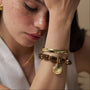 Woman wearing a gold bangle and a beaded bracelet with a gold seashell charm.