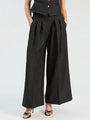 Woman wearing black wide-leg pleated trousers with subtle shimmer and a black vest.